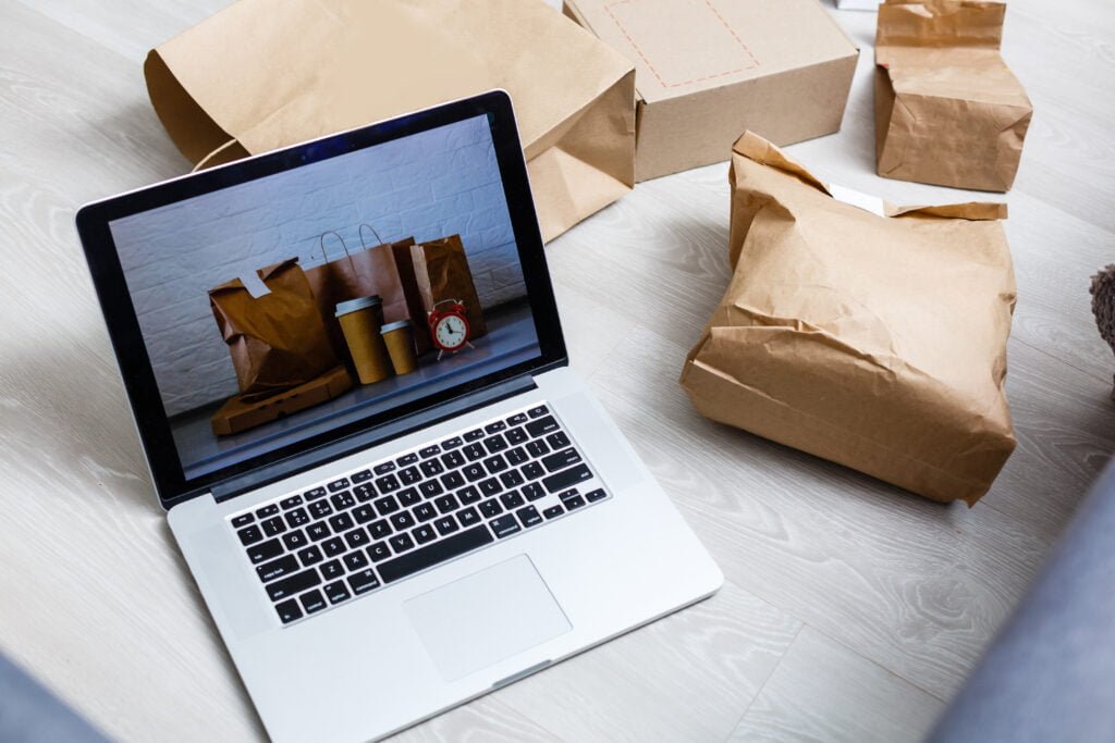 Online shopping / ecommerce and delivery service concept : Paper cartons with a shopping cart or trolley logo on a laptop keyboard, depicts customers order things from retailer sites via the internet.